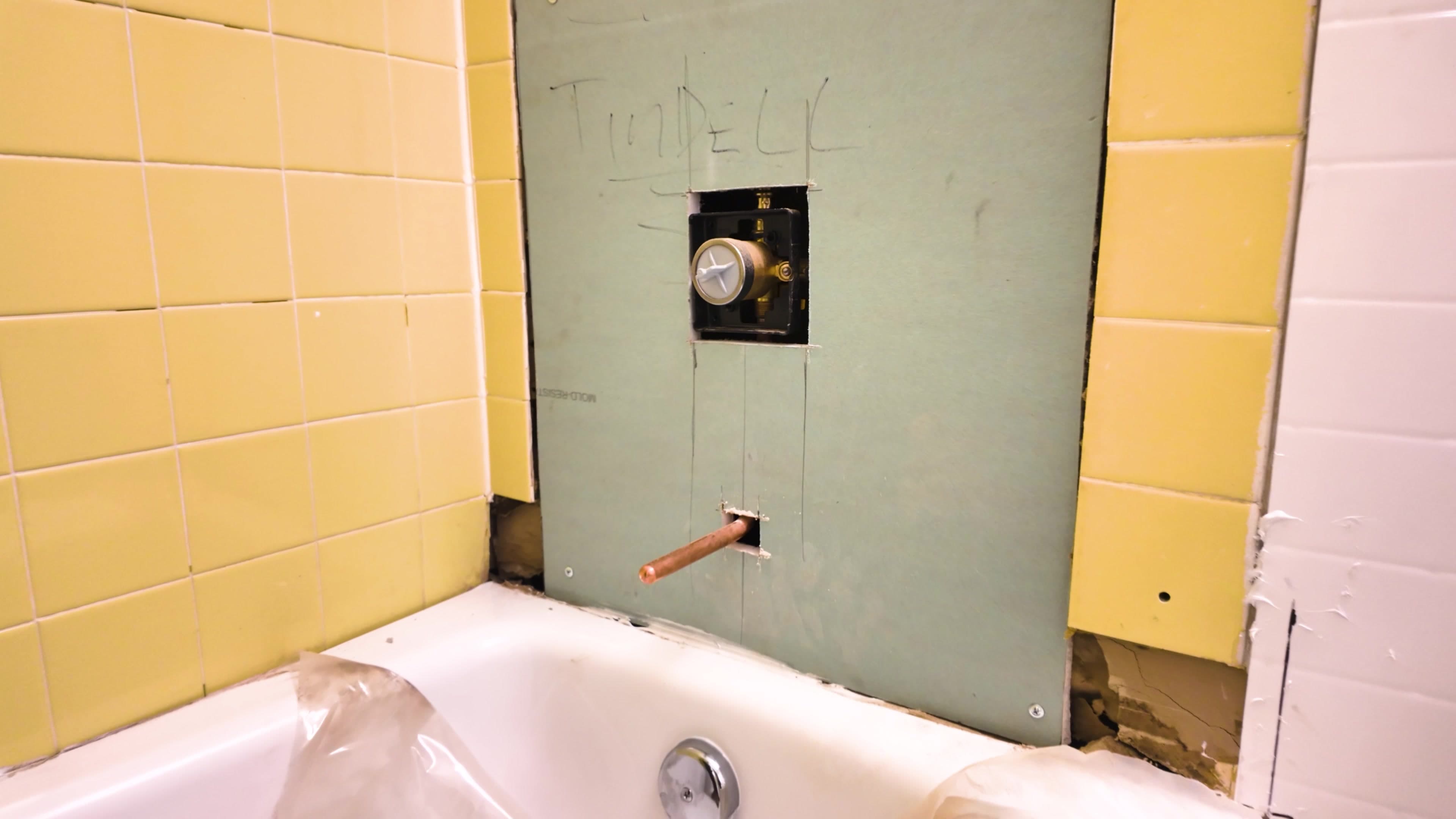 Bronx project bathroom before Tindel's new wall-system installation, showing the original yellow tile and exposed plumbing preparation
